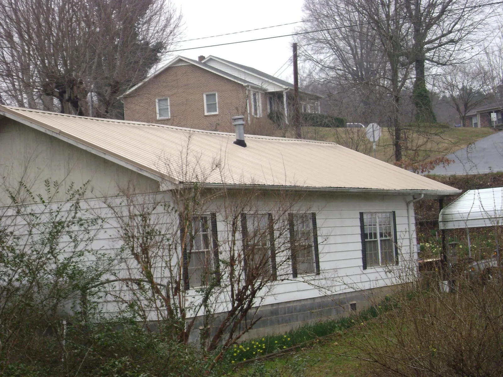 Tan metal roof on a white sided house set into a hillside — Commercial Roofing by Roofing Brothers in Tracy